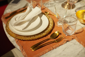 Festive christmas table setting with white and gold color plates, tableware, glasses and candles and holiday season decor.	