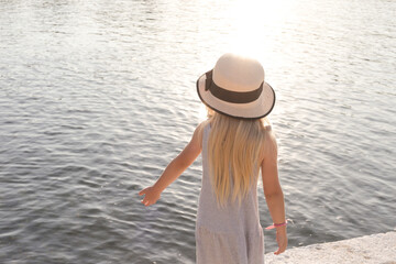 Cute little girl with straw hats looking at the sea horizon, idyllic summer vacation concept, childhood memories