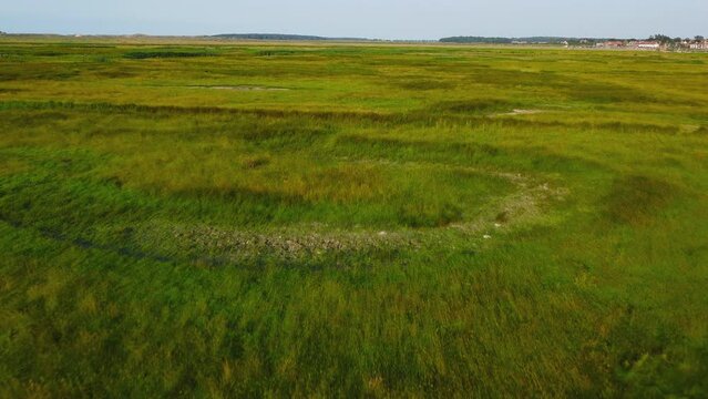 Aerial Drone Shot Flying Over Green Salt Marsh with Burnham Overy Staithe in Background in North Norfolk UK
