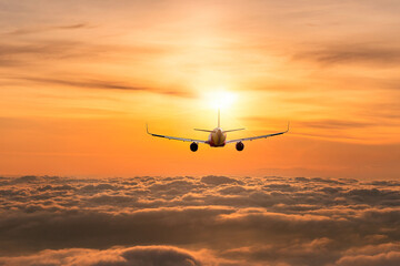 Silhouette air plane flying above fog white clouds against sun light of sunset sky background.