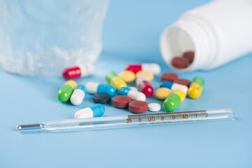 Medical mercury thermometer and pills on blue background