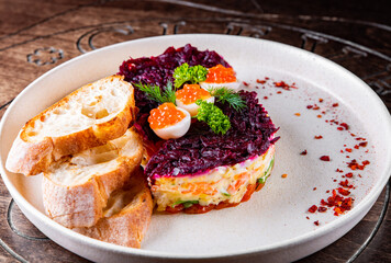 Layered salad with salmon, beets, carrots, onions, potatoes and eggs on a plate.
