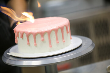pastry chef making a pink dripping frosted cake for baby girl birthday celebration at kitchen lab