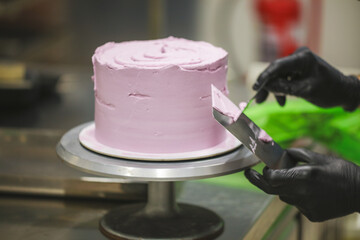 Decorator using spatula and scraper smoothing and levelling purple lilac buttercream frosted dark chocolate cake