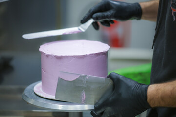 Decorator using spatula and scraper smoothing and levelling purple lilac buttercream frosted dark...