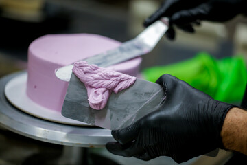 Decorator using spatula and scraper smoothing lilac buttercream birthday frosted cake