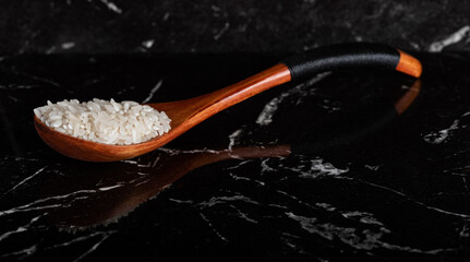 Rice in a beautiful wooden spoon on a black marble kitchen table