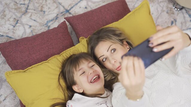 Little girl and her mother are taking pictures on the phone, making cute and funny gestures. Mother-daughter relationship.