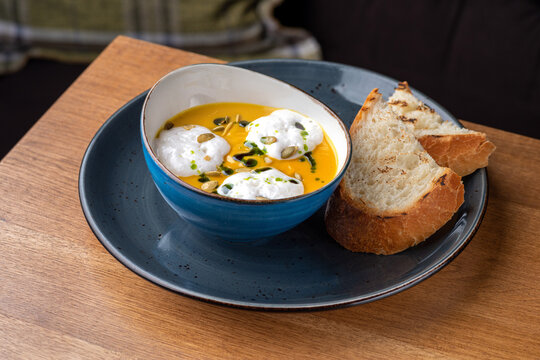 Hot Pumpkin cream soup with coconut espuma and bread on a wooden table. Healthy food
