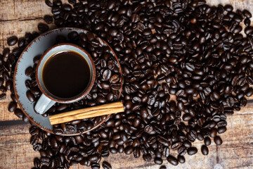 a cup of coffee with roasted beans and cinnamon on a wooden background, photographed from the top
