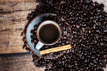a cup of coffee with roasted beans and cinnamon on a wooden background, photographed from the top