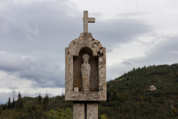 Weathered Stone Wayside Shrine with Cross and Statue in Rural Hills
