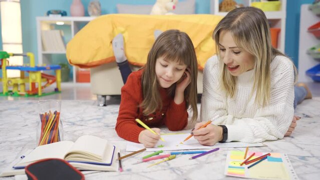 The talented little girl draws pictures with her mother in her room at home, they have fun and they have joyful moments.