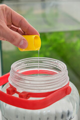 Close up of a hand adding fish tank water conditioner to fill freshwater aquarium. Fish tank maintenance.