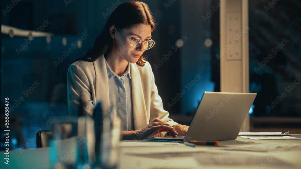 Poster stylish female working on laptop computer in a company office in the evening. young project manager 