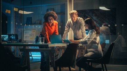 Diverse Team of Young Managers Discussing Work at a Meeting in Office at Night. Successful Business Partners Talking About a Marketing Campaign, Getting Familiar with Company Reports