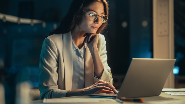 Close Up Portrait of a Young Accountant Working in the Office Late in the Evening. Positive Female Using Laptop Computer, Preparing Job Assignment and Corporate Report for Finance Director.