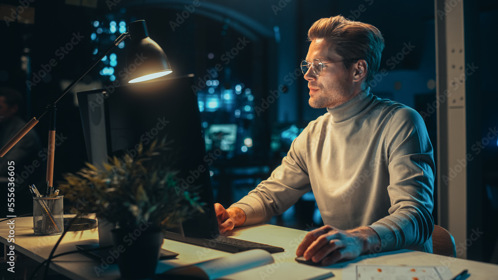 Poster Handsome Man Working on Desktop Computer in a Company Office at Night. Young Specialist Analyzing Reports. Marketing Assistant Developing a Consumer Sales Strategy for a Client.