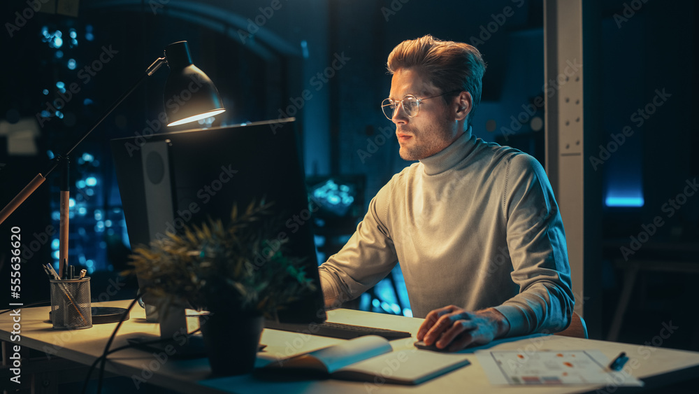 Poster handsome man working on desktop computer in a company office at night. young specialist analyzing re