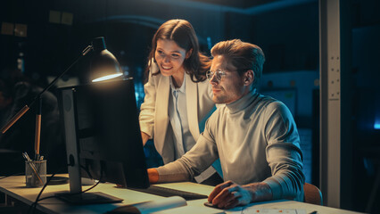 Software Developer Working on Desktop Computer in the Evening in Office. Young Female Project Manager Comes Over to the Desk to Discuss Updates to the New Online Application.
