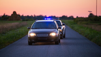 Highway Traffic Patrol Car in Pursuit of Criminal Vehicle, Speeding up the Road. Police Officers Chasing Suspect on Road, Sirens Blazing, Dust Flying. Stylish Cinematic Shot of Energetic Action Scene © Gorodenkoff