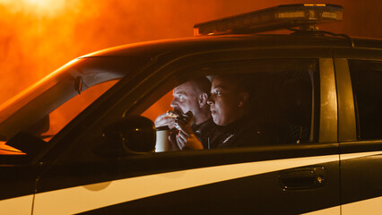 Portrait of Two Police Patrol Officers Sitting in the Car Eating Donuts, Watching Over the Streets...