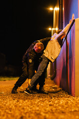 A Professional Middle Aged Policeman Performing a Pat-Down Search on a Fellon in Empty Back Alley....