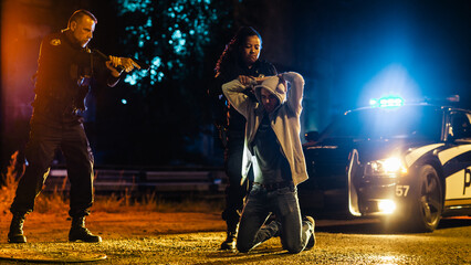 Black Female Police Officers Handcuffing a Compliant Suspect While her Male Partner Intimidats and Threatens the Criminal by Aiming a Gun at Him. Aesthetic Action Movie Shot