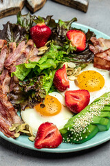 Ketogenic diet food, Fried egg bacon with avocado, strawberries and fresh salad on a light background. healthy meal concept, top view
