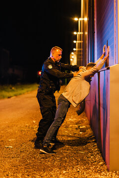 A Professional Middle Aged Policeman Performing a Pat-Down Search on a Fellon in Empty Back Alley. Documentary-like Shot of Proper Procedure of Arresting Suspects. Experienced Cop Looking for Weapons