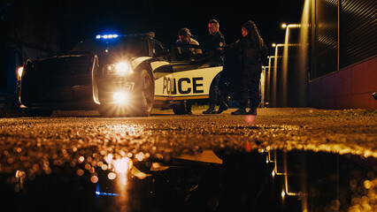 Two Police Officers Arrest Suspect, Put Him on a Patrol Сar Hood. Officers of the Law Handcuff Dangerous Criminal on Dark City Street. Cops Fight Crime. Cinematic Documentary Low Angle Shot © Gorodenkoff