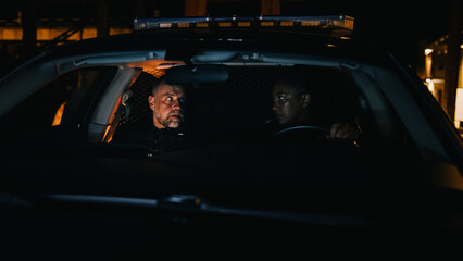 Two Multiethnic Police Officers Discussing While Waiting in the Car. Black Professional Policewoman...