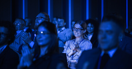 Young Woman Sitting in a Crowded Audience at a Business Conference. Female Attendee Cheering and...