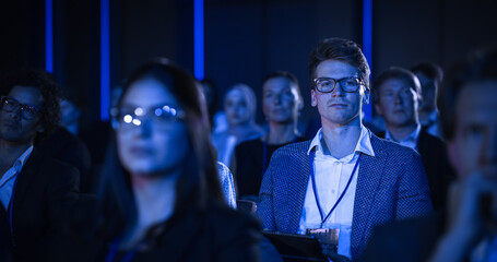 Young Man Sitting in a Crowded Audience at a Business Conference. Corporate Delegate Watching...