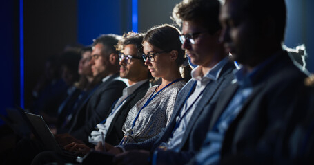 Obraz premium Young Woman Sitting in Crowded Audience at Human Resource Conference. Female Delegate Using Laptop Computer. HR Manager Listening to Inspirational Entrepreneurship Presentation About Social Studies.
