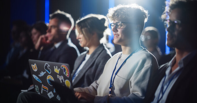 Young Handsome Man Sitting in a Crowded Audience at an International Social Studies Conference. LGBT Activist Watching Inspirational Presentation While Taking Notes on Laptop Computer.