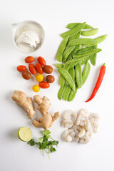 Ingredients for a spicy thai coconut soup or curry: cherry tomatoes, snow pea, chili pepper, lime, ginger, shrimps and fresh cilantro