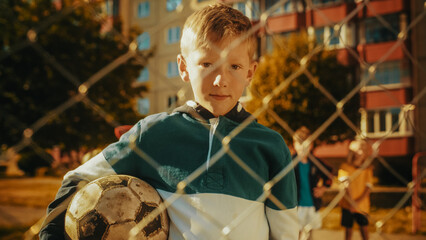 Portrait of a Cute Boy in Green and White Hoodie Holding a Soccer Ball on an Outdoors Field in the...