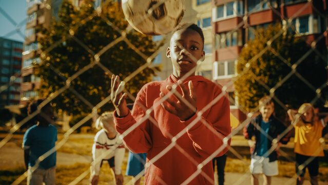 Portrait Of A Young Handsome Black Boy Throwing And Catching A Soccer Ball While Looking At Camera And Smiling. Sporty African Kid Dreaming On Becoming A Professional Football Player.