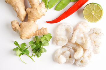 Ingredients for a spicy thai coconut soup or curry: cherry tomatoes, snow pea, chili pepper, lime, ginger, shrimps and fresh cilantro