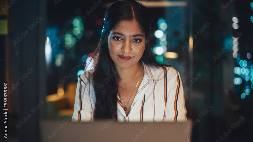 Poster young diverse accountant working in the office late in the evening. positive female using laptop com