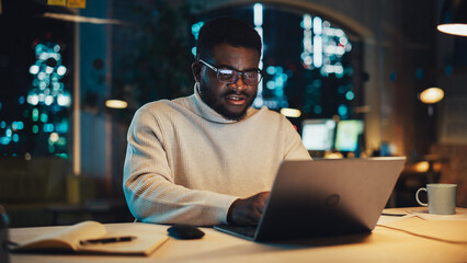 Slightly Agitated Male Employee Working on Laptop Computer in Office During Evening Time. Diverse Black African Specialist Browsing Internet, Researching Financial Data, Answering to a Work Email.