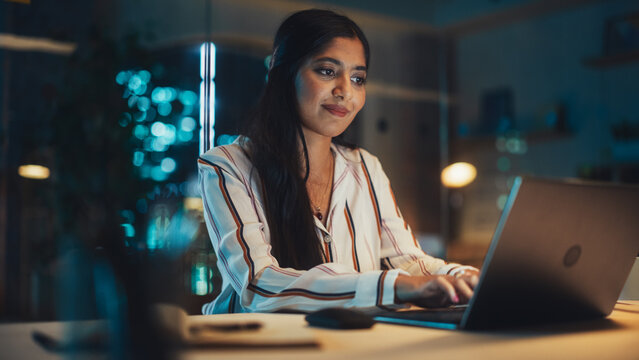 Portrait of a Happy Indian Manager Working in Creative Office. Business-Driven Stylish Female with Long Dark Hair Using Laptop Computer for Making Online Work and Writing Financial Reports. - Powered by Adobe