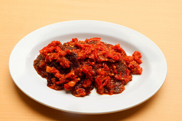 Dendeng balado or jerky beef with spicy seasoning is a traditional cuisine from west sumatera, indonesia. it is made from slice of beef with spicy sauce called sambal. served on plate.