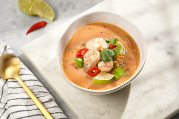 a spicy thai coconut soup or curry made of coconut milk, cherry tomatoes, snow pea, chili pepper, lime, ginger, shrimps and fresh cilantro on marble board on grey concrete background