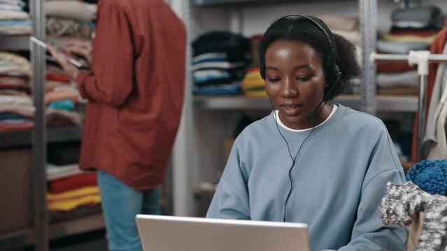 Multiracial woman wearing operator headset working at online clothes shop center. Female manager working at home office. Small business and call center concept