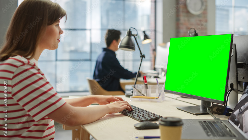 Wall mural portrait of white young female using a computer with green screen display in a spacious bright offic