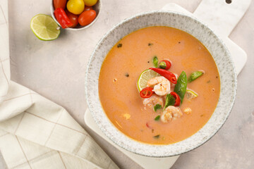 a spicy thai coconut soup or curry made of coconut milk, cherry tomatoes, snow pea, chili pepper, lime, ginger, shrimps and fresh cilantro on marble board on grey concrete background