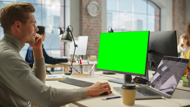 Portrait of White Creative Young Man Working on Green Screen Computer During the Day in Modern Busy Office. Project Manager Smiling While Using Desktop Computer.