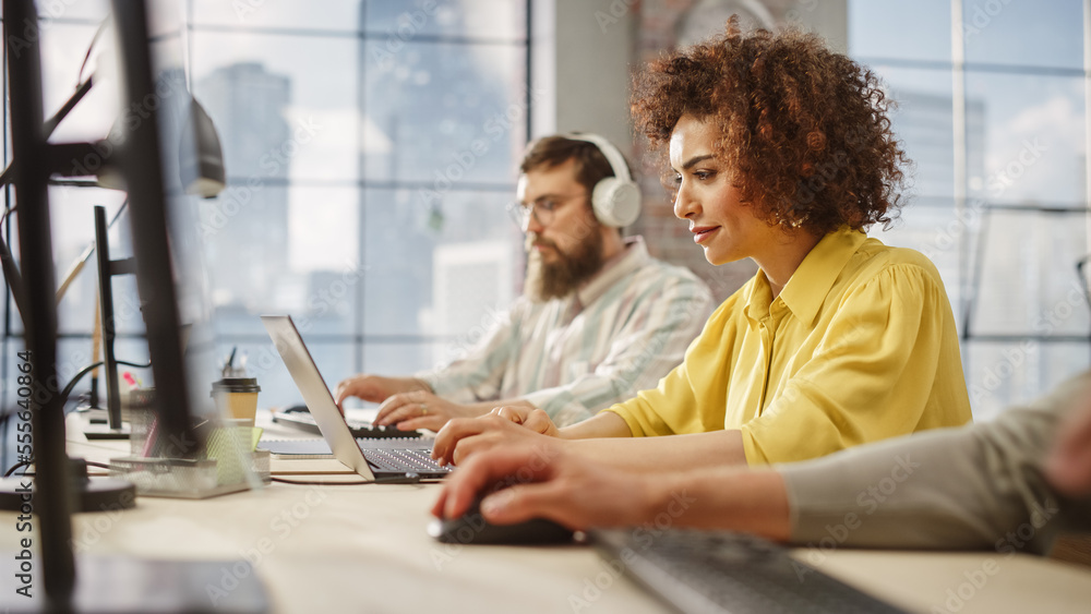 Poster portrait of creative biracial woman focused on work while using a laptop in a busy office. female gr